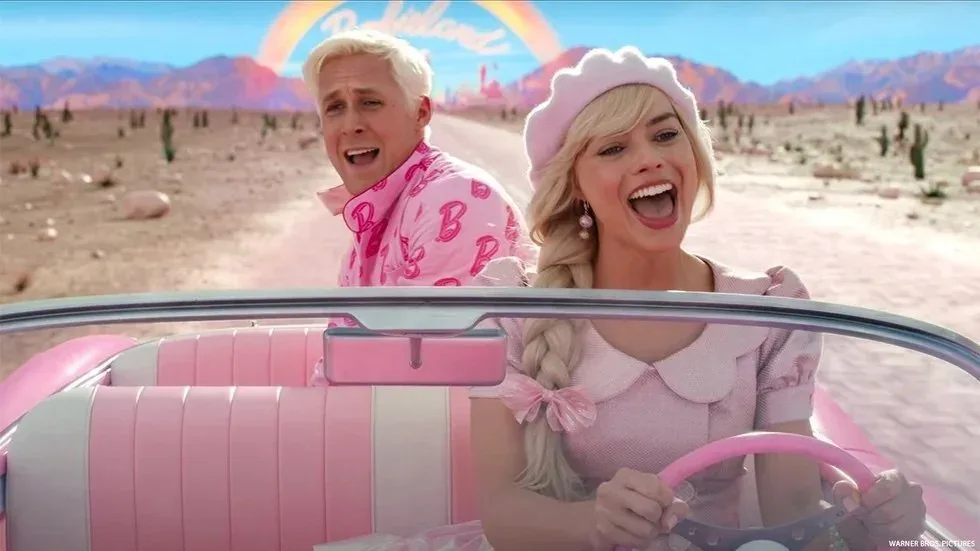 Film still from Barbie of two characters riding in a convertible through a desert landscape.